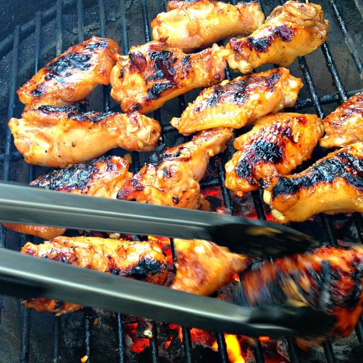 Chicken on a barbecue grill with tongues turning a piece.